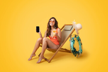 Happy millennial asian lady in swimsuit, sunglasses with inflatable ring sit on deck chair, enjoy tropical cocktail