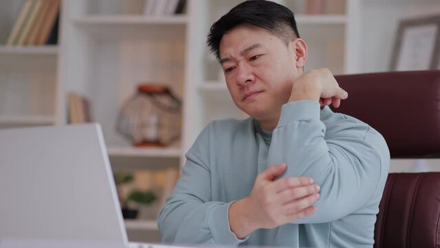 Pain in elbow. Asian man at computer workplace and experiencing pain and discomfort in elbow joint. Arthritis, orthosis, bursitis concept Pain in elbow. Arthritis, orthosis, bursitis concept