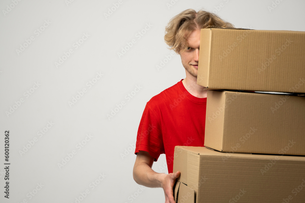 Wall mural Courier in a red uniform holding a stack of cardboard boxes. Delivery man delivering postal packages over white studio background.