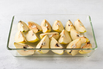 Quartered quince in a glass baking dish on a light gray background. Stage of preparation of vegan pastila or other dessert