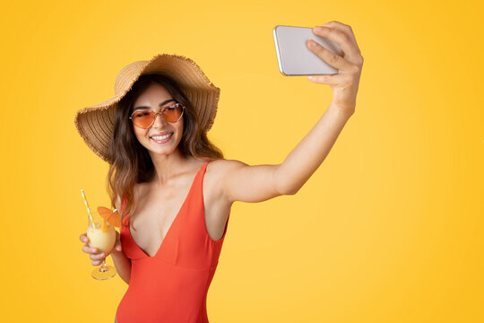 Smiling millennial asian woman in swimsuit, sunglasses and hat with tropical cocktail, enjoy free time