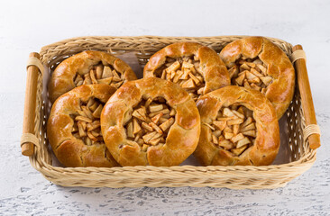 Sweet mini pies with apples and cinnamon in a wicker basket on a light gray background. Delicious homemade food