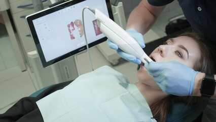 Doctor scans the patient's teeth in the clinic. The dentist holds in his hand a manual 3D scanner for the jaw and mouth. Dental health. Creates a 3D model of teeth and gums on a medical monitor