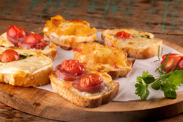collection of bruschetta baked in slices of bread with melted cheese, cherry tomatoes on cattails on wooden table at an angle in close-up from the front