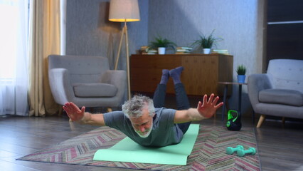 Portrait of a gray-haired senior man with a beard. Doing exercises on fitness mat. Grandfather...