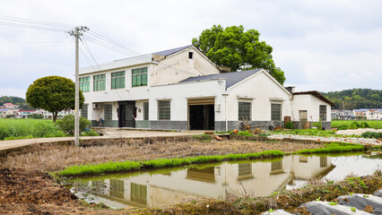 White Village house under moving clouds, with reflection in water pond, in Hunan Province, China