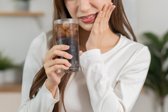 Health asian young woman, girl hand touching her mouth, suffering from toothache, decay or sensitivity cavity molar tooth or inflammation drink cold, sparkling water at home. Sensitive teeth concept.