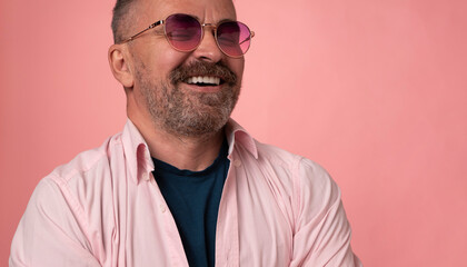 Portrait of a successful handsome smiling mature man in rose glasses dressed in pastel pink shirt isolated on pink background. handsome bristle man face with big white smile
