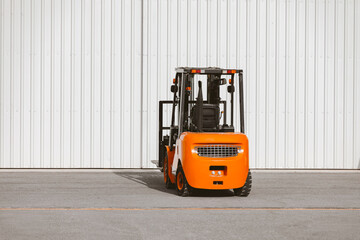Forklift, reliable heavy loader parked next to the gates of hangar. Industrial vehicle.