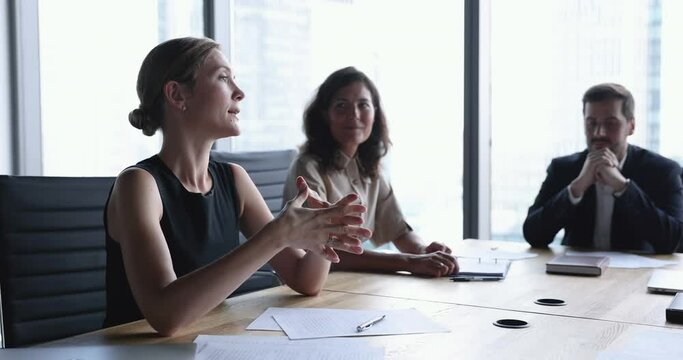 Business partners negotiating in board room. Attractive female, company head lead formal meeting with clients or shareholders, make speech, explain contract details seated at desk in conference room