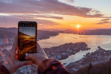 Female hands taking photo of sunset over a seaside city and harbor on a phone