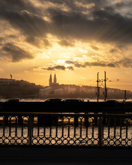 As the sun sets, casting golden rays across the sky, a striking yellow and black photograph captures the enchanting silhouette of a castle in the background. In the foreground, the silhouettes of cars