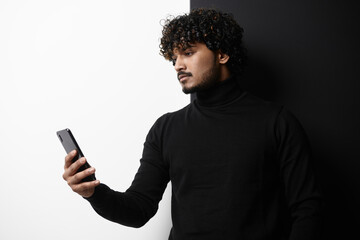 Handsome Indian man using smart phone while standing against black and white background