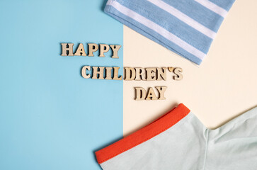 happy childrens day inscription formed from wooden letters.happy has shape of smile.t shirt sleeves for kids.blue and ivory background, wooden eco toys mock up.red collar as smile.child clothes