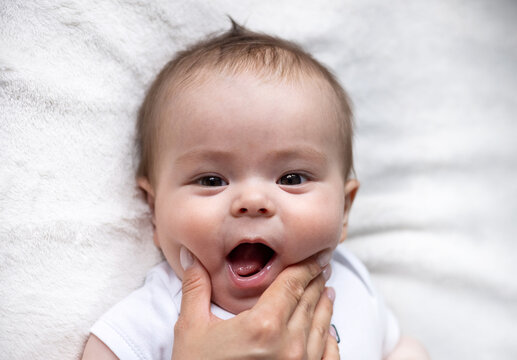 Baby Lying On Bed Holding Feet With Small Hands, Tongue Out Smiling Profile Side View.toddler Infant Playing With Soft Toy For Teething.top View.adorable Boy On Bed.mother Push Checks With Fingers