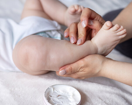 mother hand using cream from jar to apply on baby new born infant legs.child with eczema or dermatitis red spots on foot. rash or kid allergy on body.woman hand massaging putting cream on dry skin