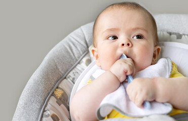 adorable cute baby boy sitting in swing cradle eating mashed food with spoon.mother hand feeding...