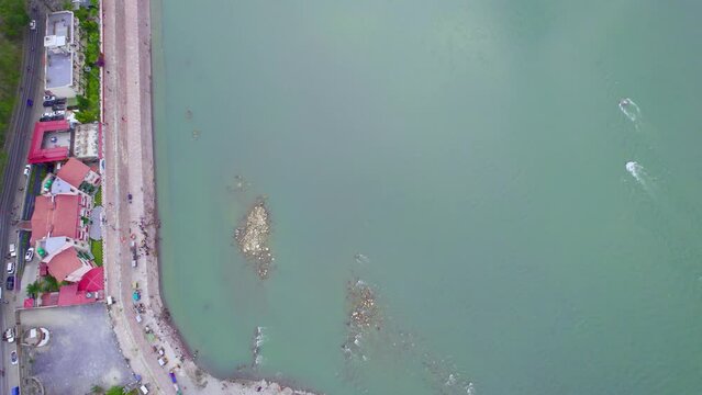 pan up aerial drone shot going from car parking, stairs on ghat river bank over blue water of ganga to temples and ram setu suspension bridge in distance in Rishikesh in between himalaya mountains