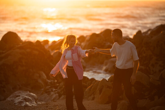 A young couple in love on the coast among the rocks in a beautiful sunset.