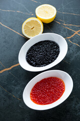 Two bowls with red and black caviar on a dark-olive marble background, vertical shot, high angle view