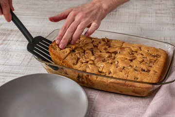 Pieces of fruit and berry pie in a glass bowl are removed with a spatula and placed on a plate. Close-up of a female hand laying pieces of apple pie on a plate. The concept of cooking pies