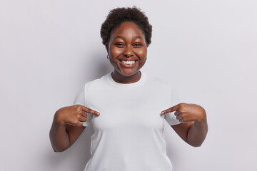Place your advertising text here. Cheerful dark skinned plump woman points at blank space of t...