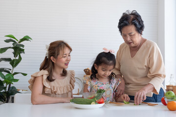 Granddaughter helping mom and grandma make salads in the kitchen. Asian family.