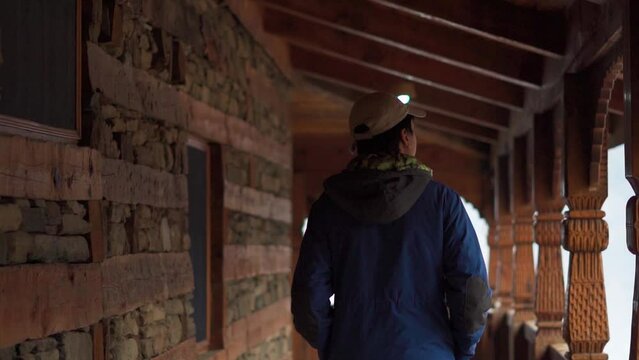 Rear view shot of an Indian man walking inside the traditional wooden house in the aisle between wall and pillars at Manali in Himachal Pradesh, India. Tourist observing the old wooden home in Manali.