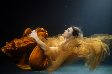Woman in dress in a state of levitation under the deep waters of the ocean