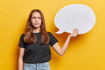 Horizontal shot of displeased long haired young woman frowns face holds speech bubble for your text...