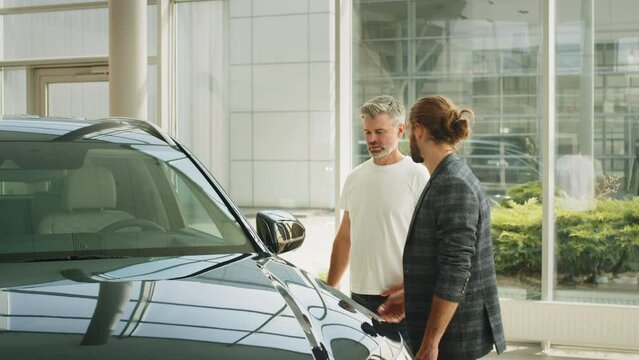 Handsome business man came to get new auto. Two men elderly father and adult son in a showroom choose a new car. Young caucasian cars salesman show the best variant to customer in dealership