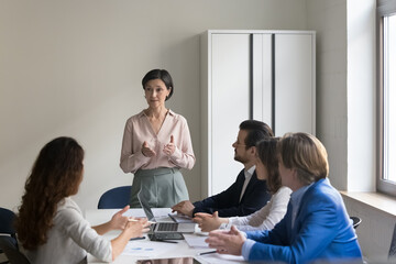 Executive team listen to mature female CEO presenting project plans for coming year, explain...