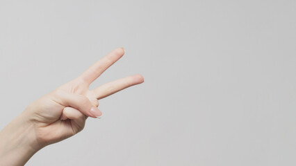 Hand gesture. Victory sign. Woman showing two fingers pointing copy space on light gray background.