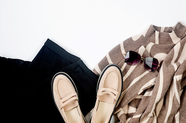 Black pants, beige knitted oversize sweater, beige suede loafer on white background.