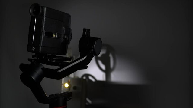 An old movie camera works on an automatic steadicam against the background of a movie projector.