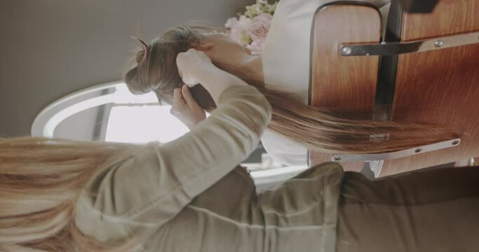 The hairdresser adds hair extensions to a brunette lady in a beauty salon. Professional hair care. Vertical video. Trucking motion