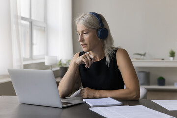 Confident positive freelance business woman in wireless headphones talking on video call,...
