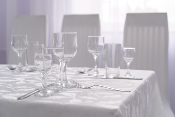 a set table with cutlery on a white tablecloth in a hall with light walls and curtains