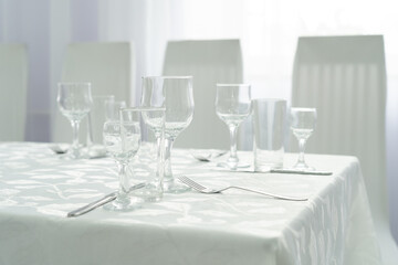 a set table with cutlery on a white tablecloth in a hall with light walls and curtains