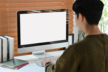 Rear view of focused man freelancer looking at computer monitor, working online at home.