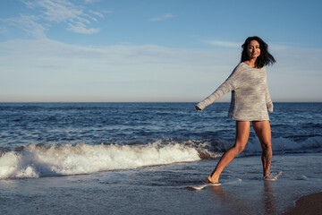 Fototapeta na wymiar young beautiful brunette girl walks on the sand on the seashore in a swimsuit and a sweater