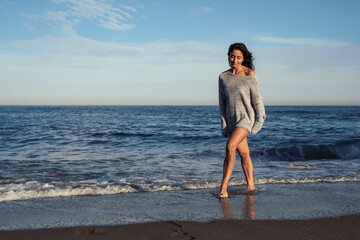 Fototapeta na wymiar young beautiful brunette girl walks on the sand on the seashore in a swimsuit and a sweater