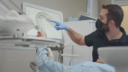 A male orthodontist doctor scans a man's teeth and jaw in the clinic's medical office. Creates a 3d...