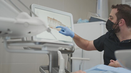 A male orthodontist doctor shows on the display a 3d model of the oral cavity of a man patient....