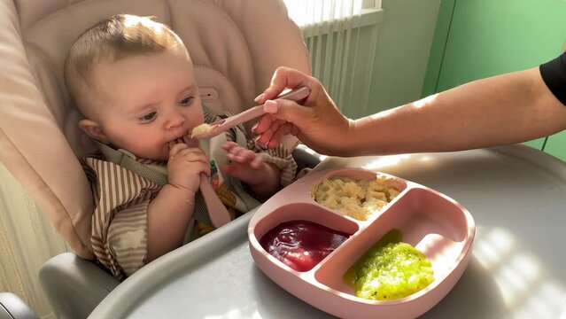 Baby spoon-feeding breakfast in the kitchen for the first time. The first meal, the beginning of feeding children