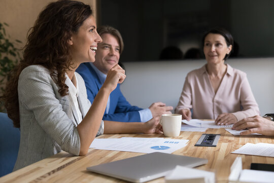 Happy Hispanic businesswoman and mature colleagues engaged in teamwork, negotiations or team building event in modern conference room, discuss project details, review sales statistics enjoy teamwork