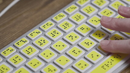 Close-up of a computer keyboard with braille. A blind girl is typing words on the buttons with her hands. Technological device for visually impaired people.