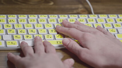 Close-up of a computer keyboard with braille. A blind girl is typing words on the buttons with her hands. Technological device for visually impaired people.