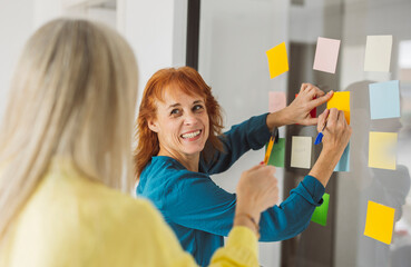 mature women at coworking, businesswoman writing in notepad during meeting in office