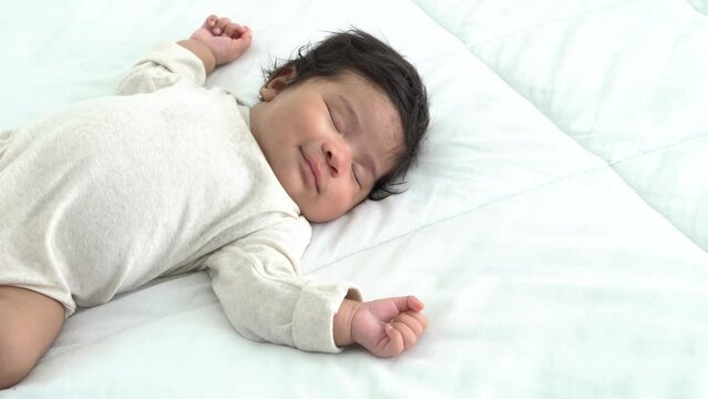 Baby is half Nigeria half Thai, 2-month-old newborn daughter, smiled as slept soundly on the white bed. to infant and family concept.	